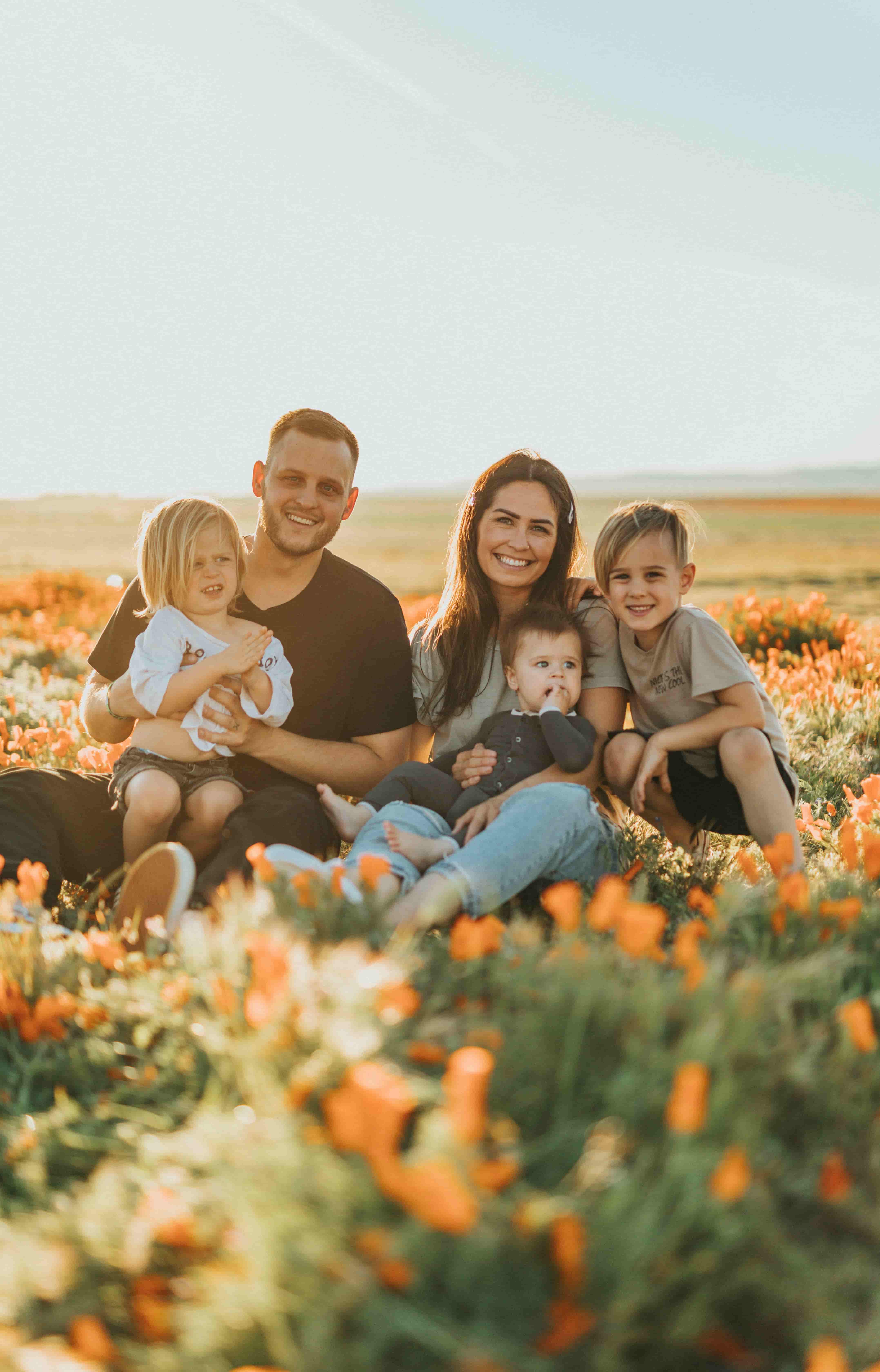 Familie mit drei Kindern sitzt lachend in einem Blumenfeld